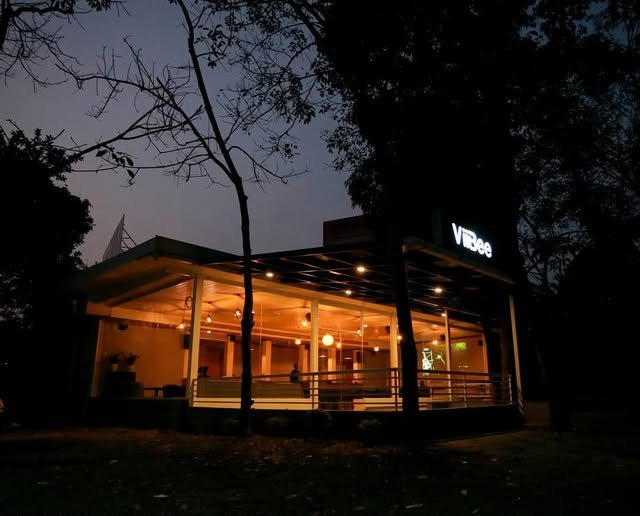 The ViiBee pavilion at dusk, lit warm under the trees, with the sky still blue behind it.